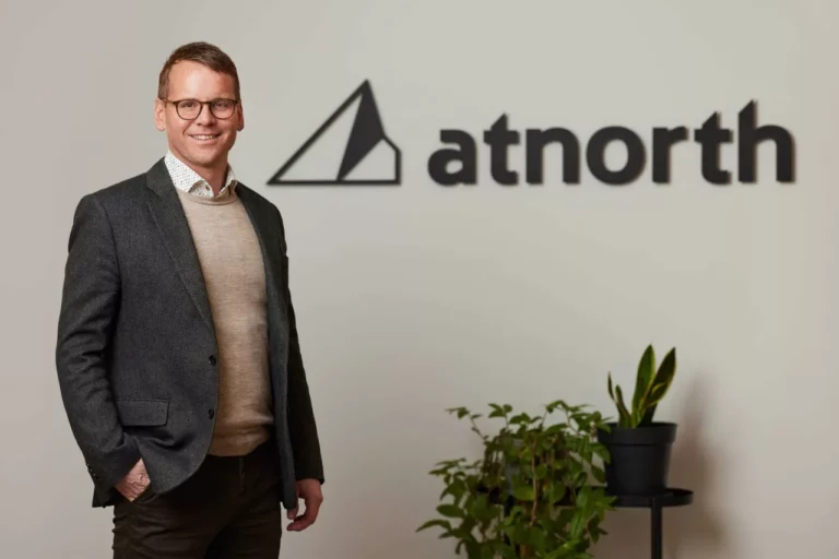 Eyjolfur Magnus stands smiling next to a potted plant with the "atnorth" logo on the wall behind him.