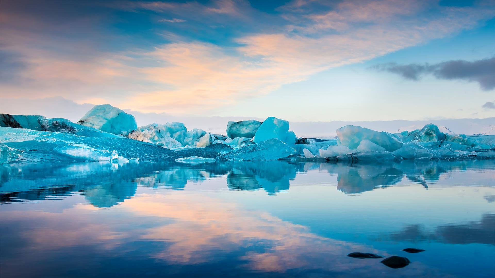 Icebergs and ice formations reflected in calm water under a pastel-colored sky.