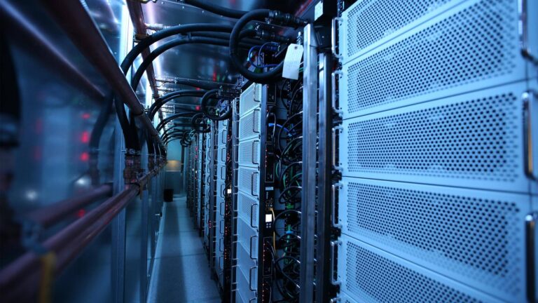 A row of computer servers in a data center, lit by blue lighting, with visible cables and ventilation panels.