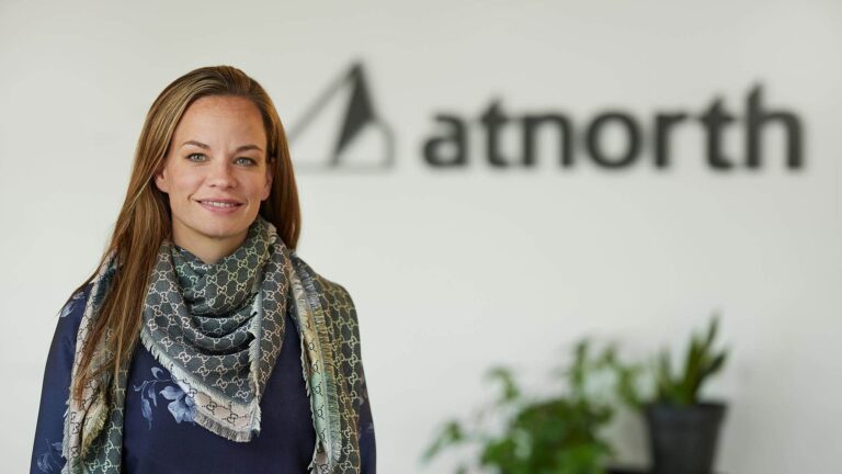 A woman stands in front of an "atnorth" logo with plants in the background.