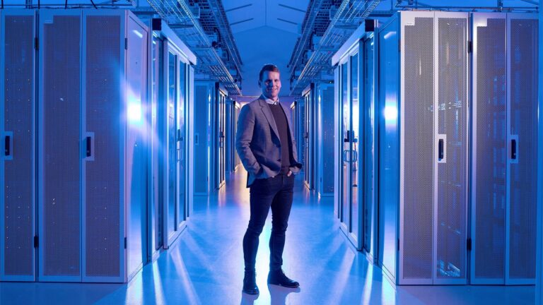 Person standing in a brightly lit data center aisle surrounded by server racks.
