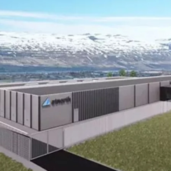 A large industrial facility, housing sustainable data centers, displays its logo prominently on the building exterior, all set against a backdrop of mountains and a partly cloudy sky.