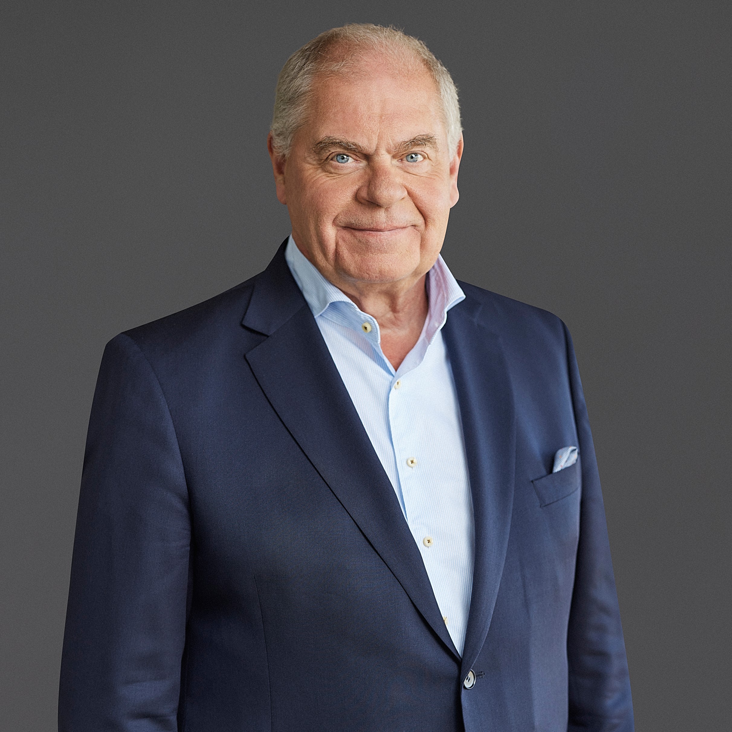 An older man in a navy suit and light blue shirt stands against a gray background, embodying the sophistication of sustainable data centers.