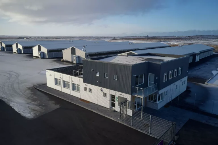 Aerial view of a sprawling industrial complex resembling a data center, with multiple gray and white buildings on a snowy landscape under a cloudy sky.
