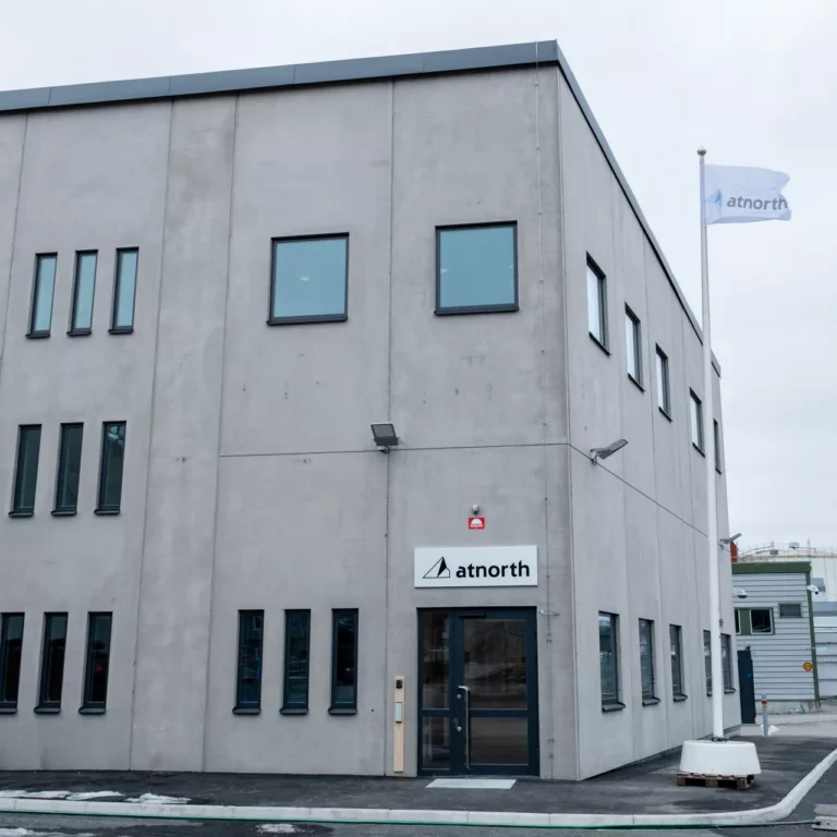 Two-story concrete building with several windows and a flagpole bearing the "atnorth" logo. The main entrance features a sign with the same logo. The sky is overcast.