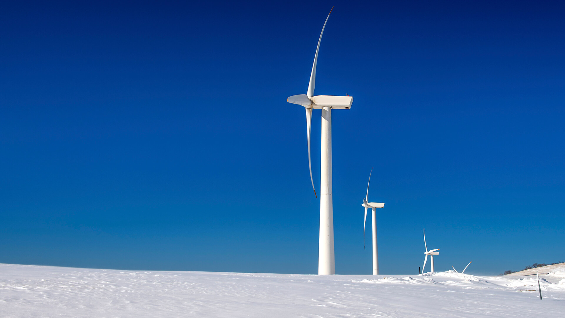 Three wind turbines stand beside a data center on a snowy landscape under a clear blue sky.