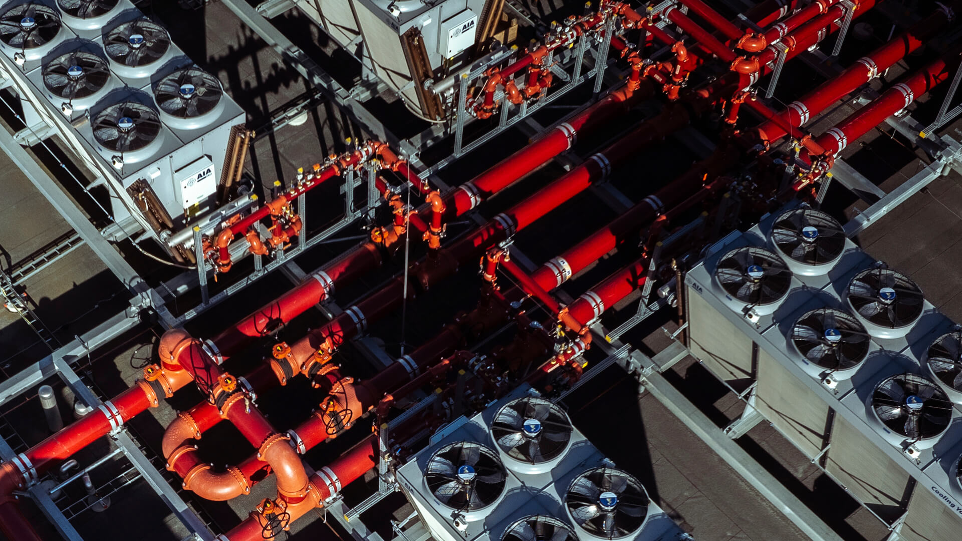 Aerial view of industrial equipment at a data center featuring interconnected red pipes, large fans, and rectangular units on a metal platform.