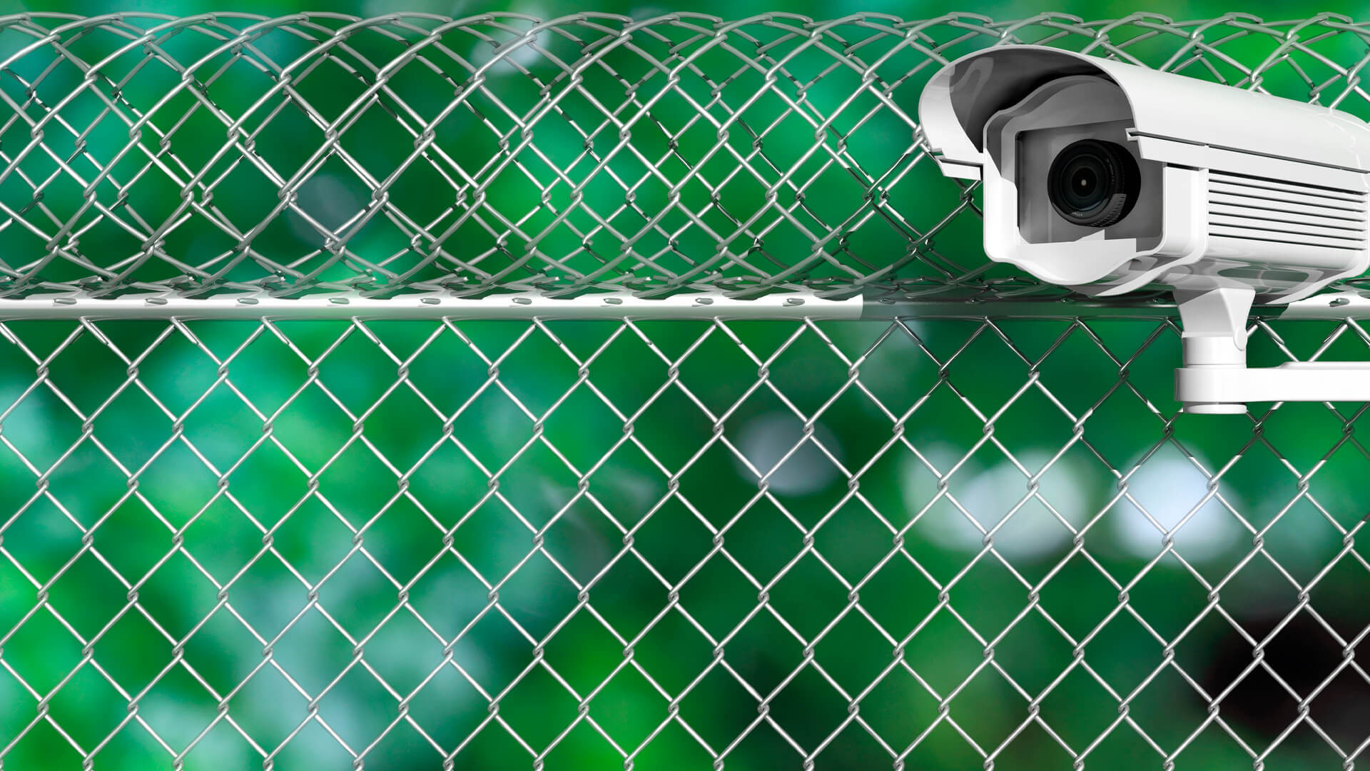 A security camera, a vigilant guardian, is mounted on a chain-link fence against a blurred green background, reminiscent of the protective measures surrounding a secure data center.