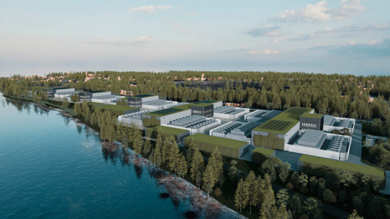 Aerial view of an industrial facility, possibly a data center, nestled among trees and located near a serene body of water, with a clear sky overhead.
