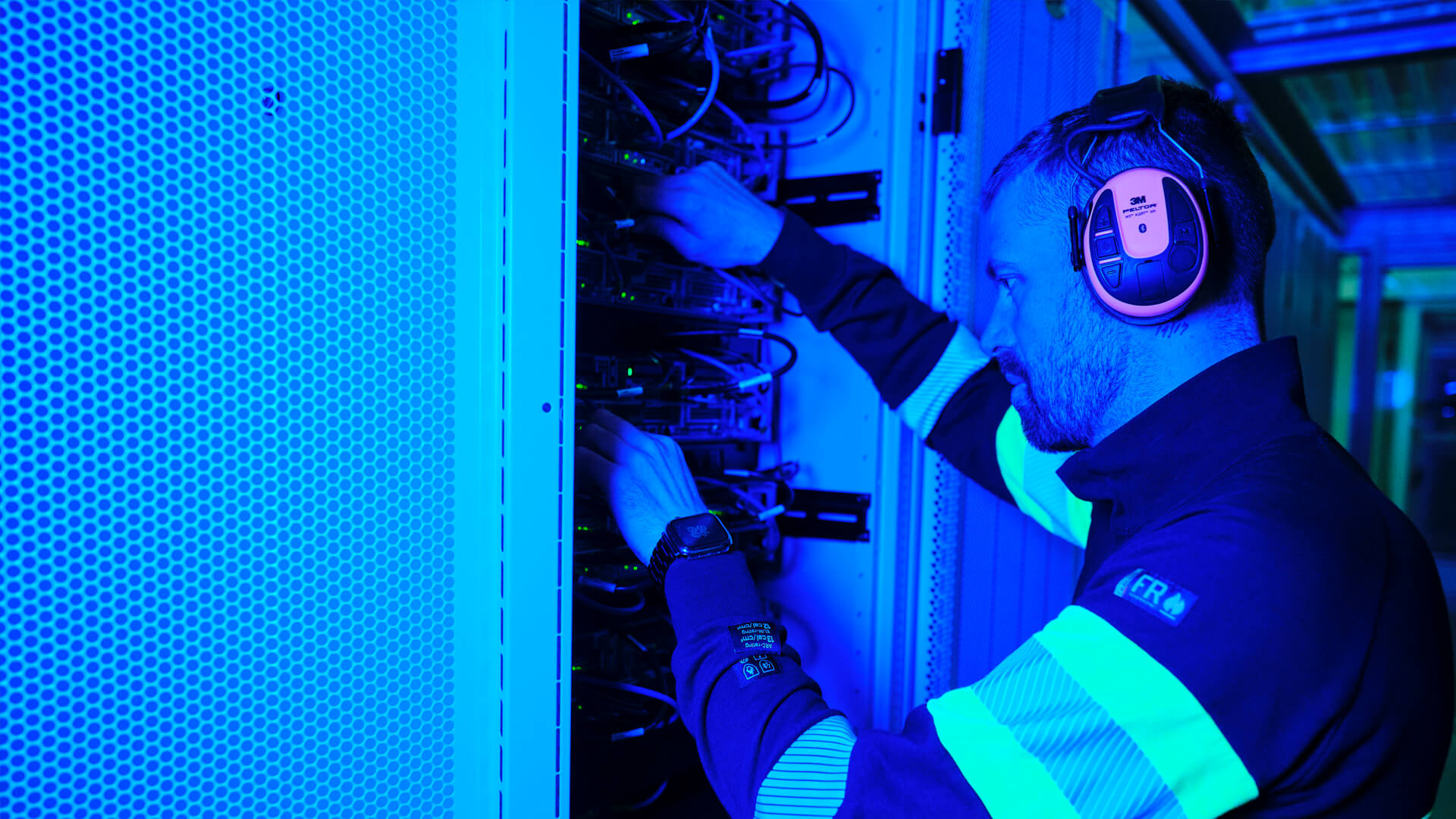 A person in protective gear meticulously tends to servers in a cutting-edge data center, illuminated by ambient blue lighting.