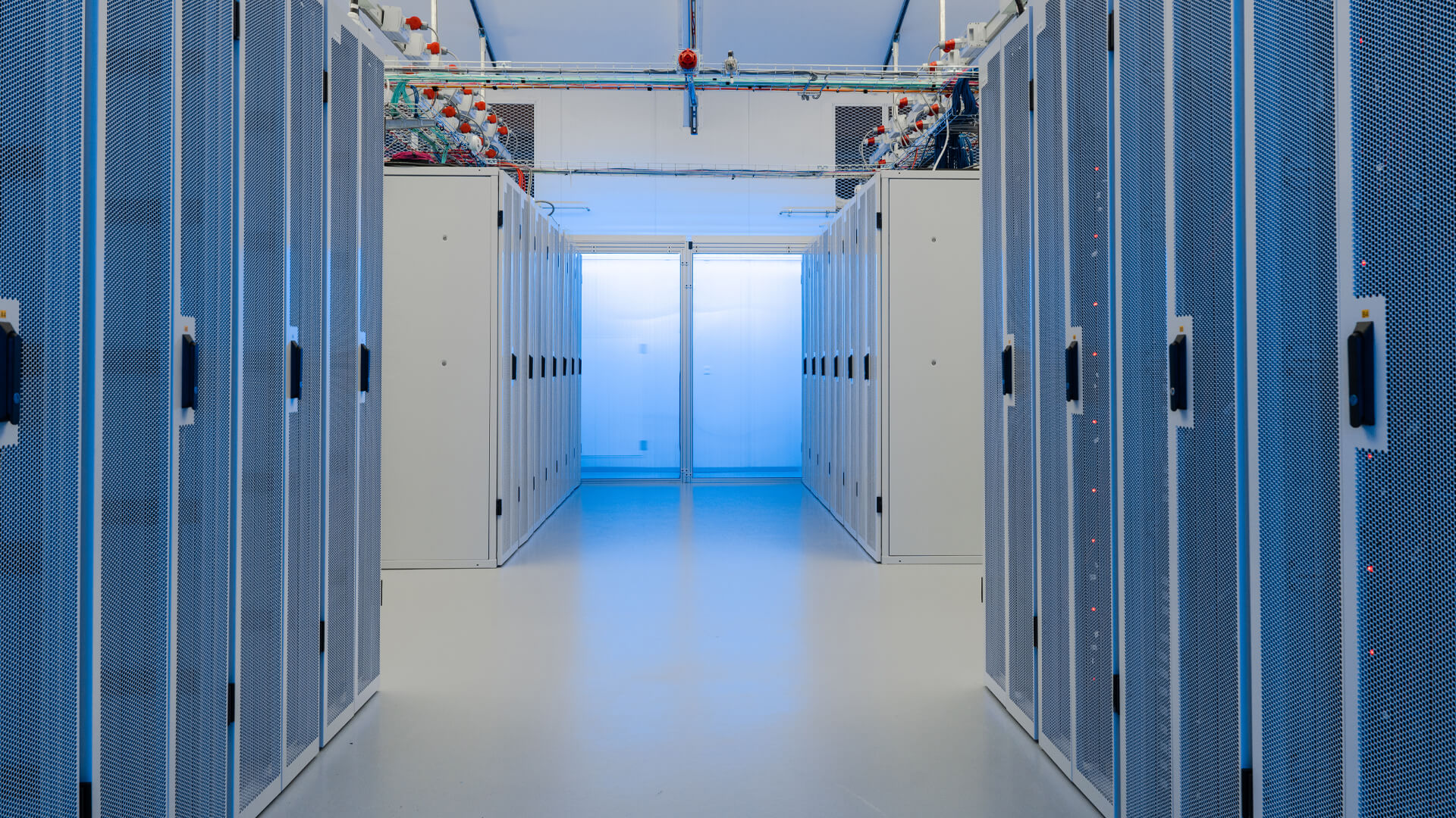 The data center's hallway stretches between rows of server racks on both sides, its path ending with a door, illuminated by the steady glow of overhead lights.