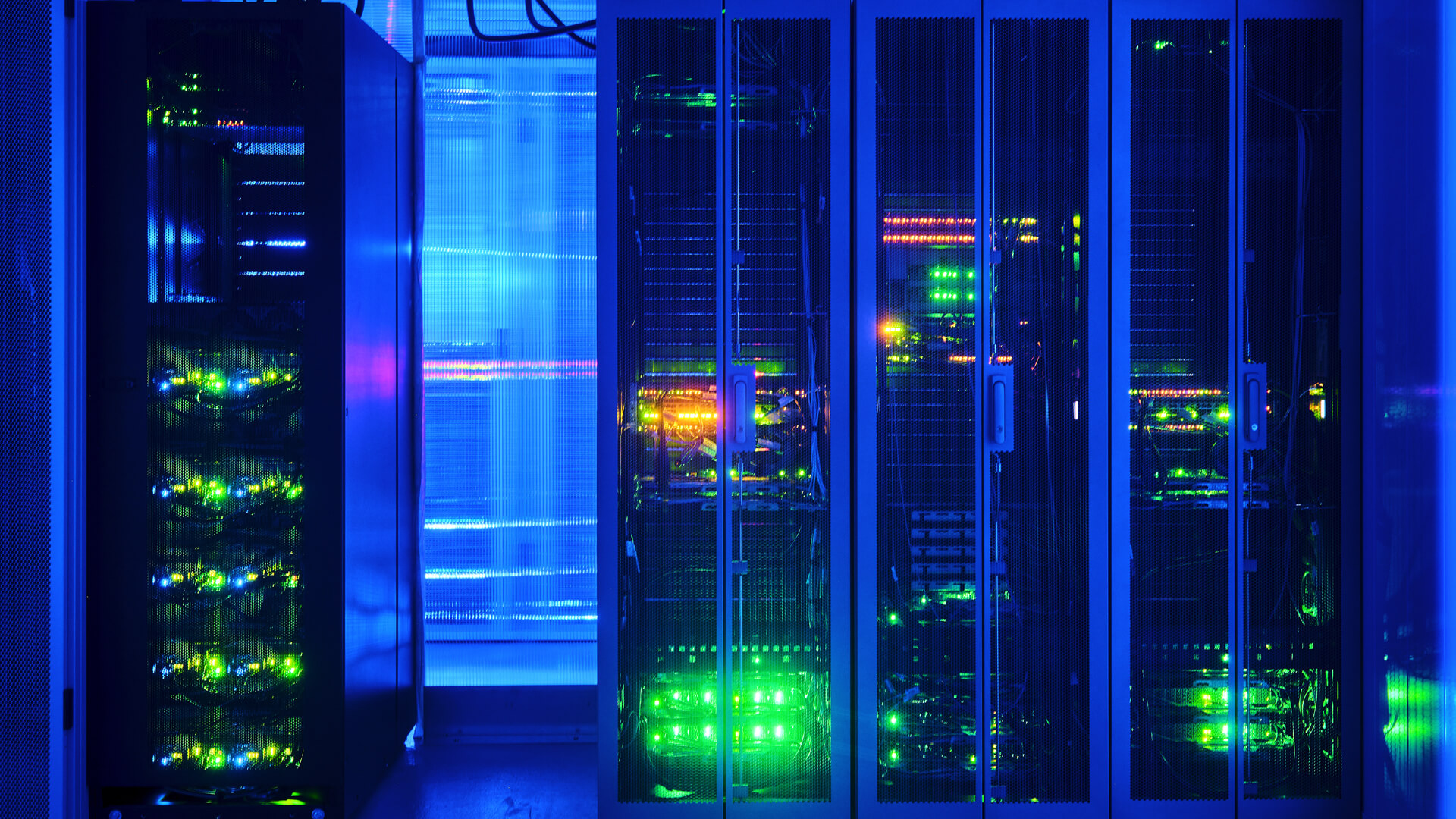 A dimly lit data center with glowing green and orange lights on several server racks.