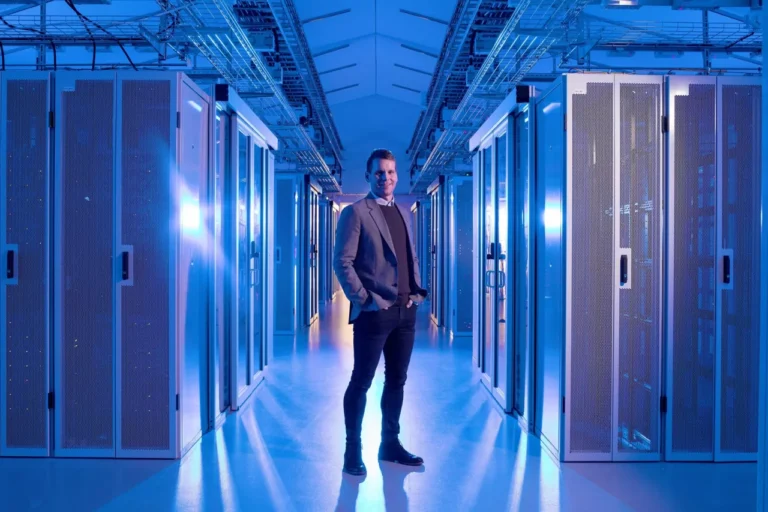 A person stands confidently in a brightly lit data center aisle, surrounded by multiple server racks on both sides, embodying the cutting-edge essence of modern technology.
