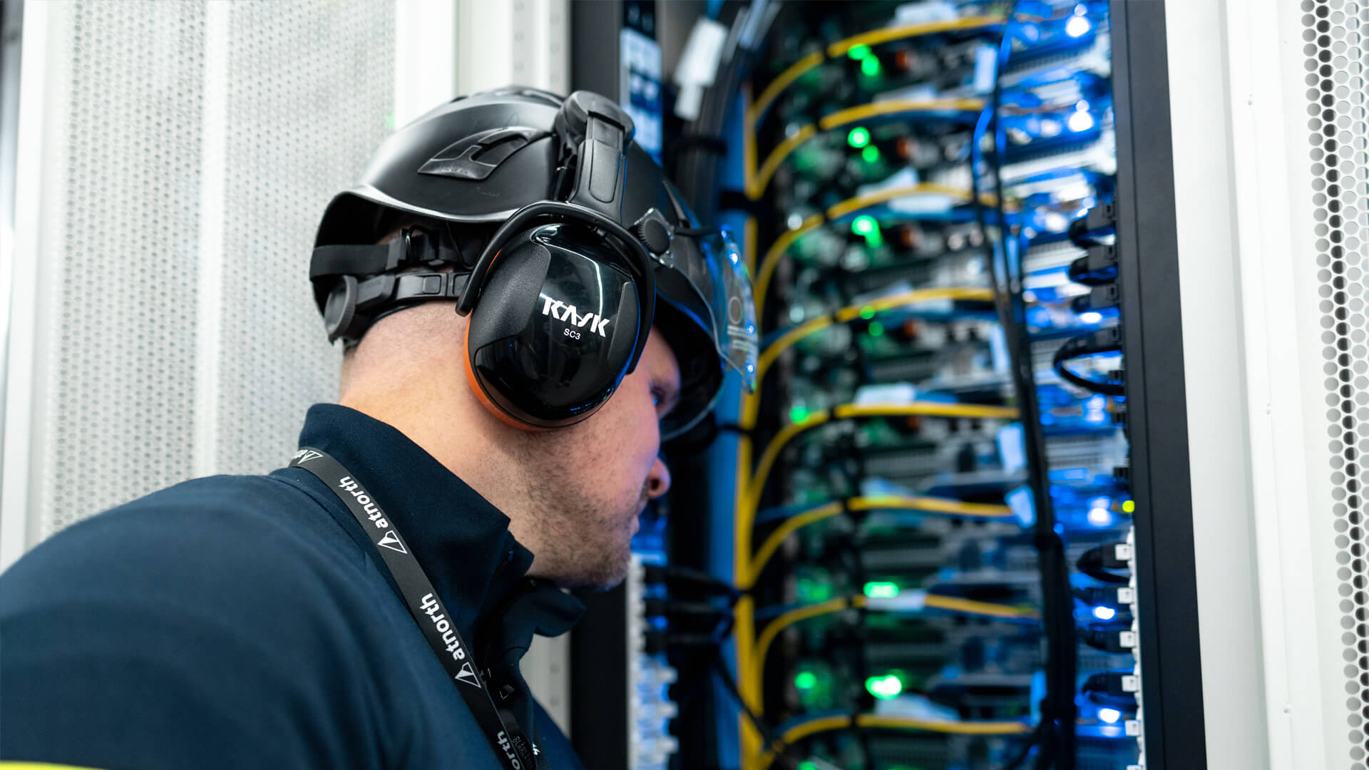 A person wearing protective gear inspects the wiring in a data center's server room.