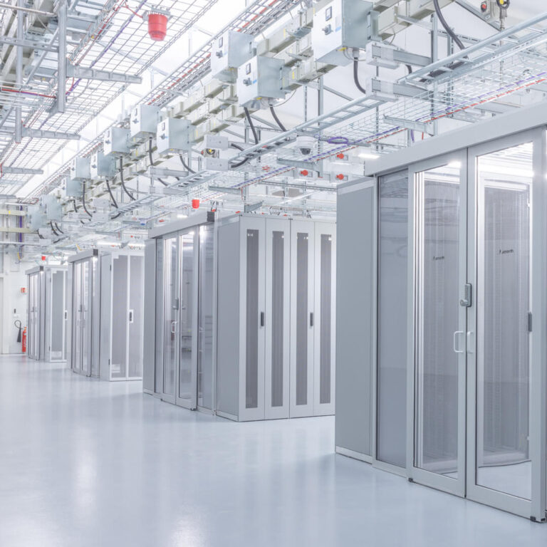 A modern, brightly lit hallway in a bustling data center reveals rows of server racks and neatly organized overhead cabling.