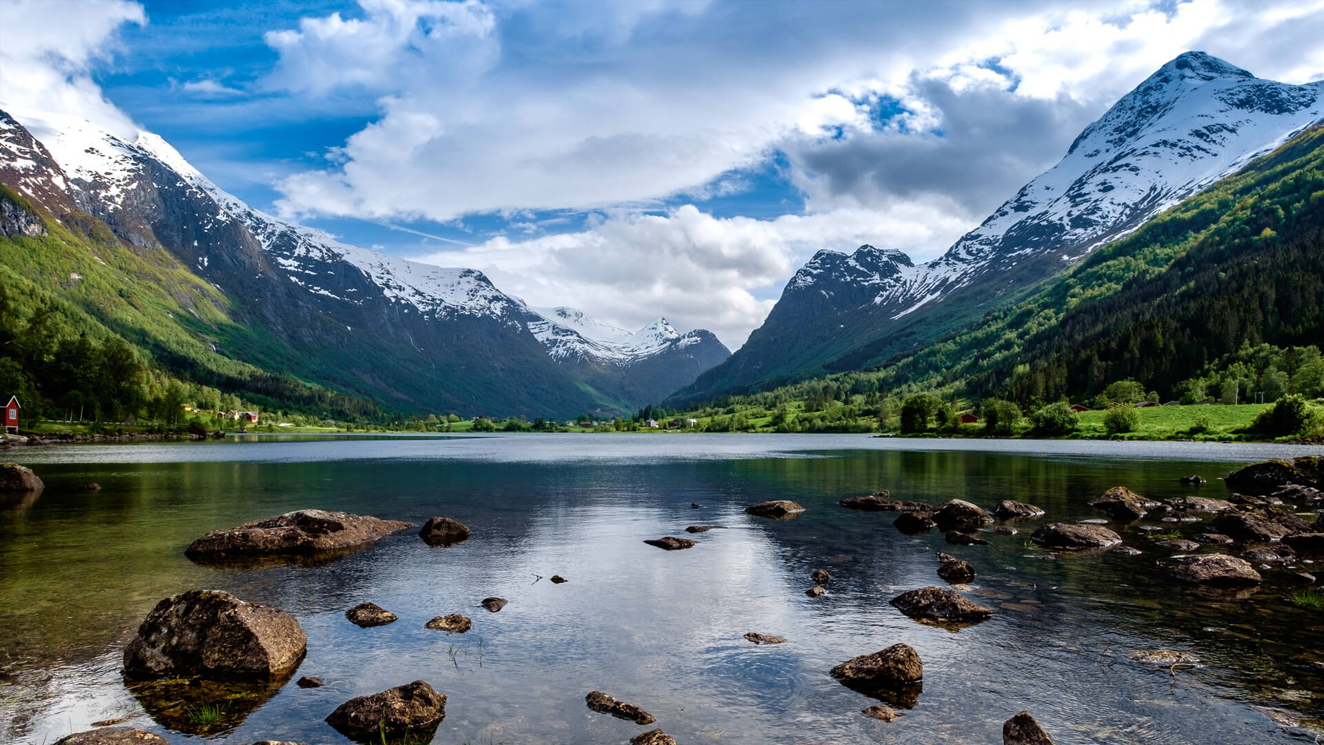 A tranquil lake, reminiscent of a serene data center, is surrounded by snow-capped mountains and lush greenery under a partially cloudy sky.
