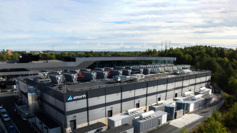 A large industrial building surrounded by greenery, with multiple rooftop units and a logo that reads "atnorth.