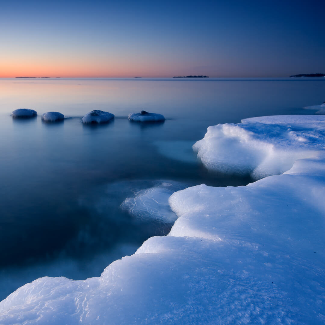 A serene winter seascape at dusk features icy formations along the shoreline, reminiscent of how sustainable data centers blend technology seamlessly with nature, while calm water reflects the fading light.