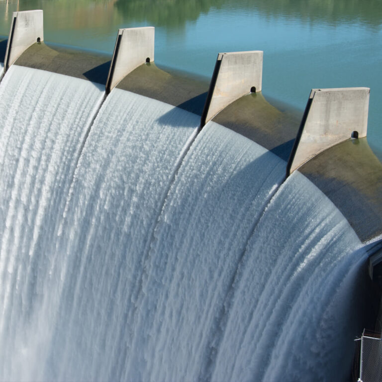 Water cascades over the edge of a large concrete dam, reminiscent of the cooling systems used in sustainable data centers, with blue water visible at the top.