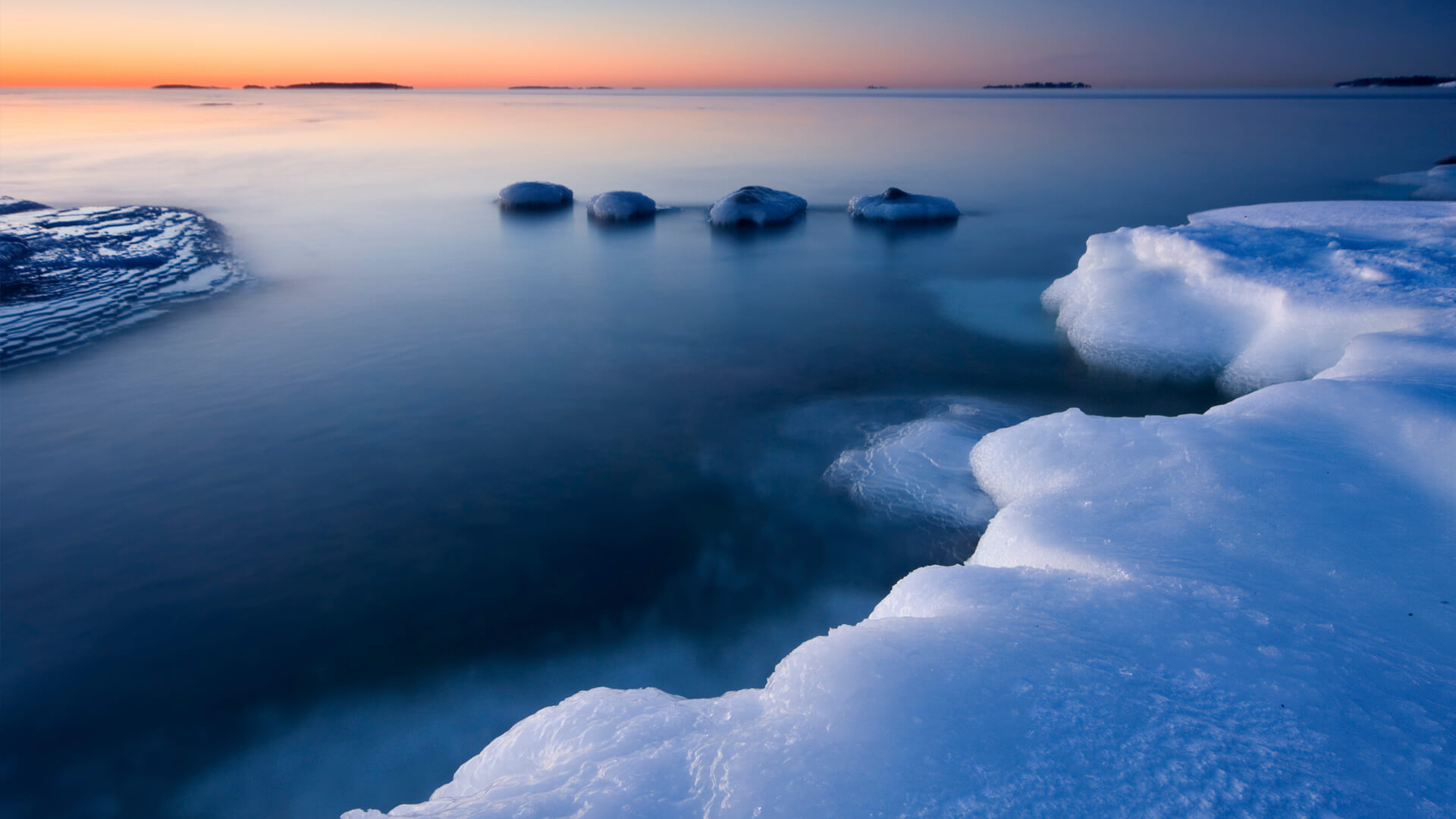 A serene view of icy shores and calm water at sunset, resembling a natural data center with patches of ice floating on the mirrored surface.