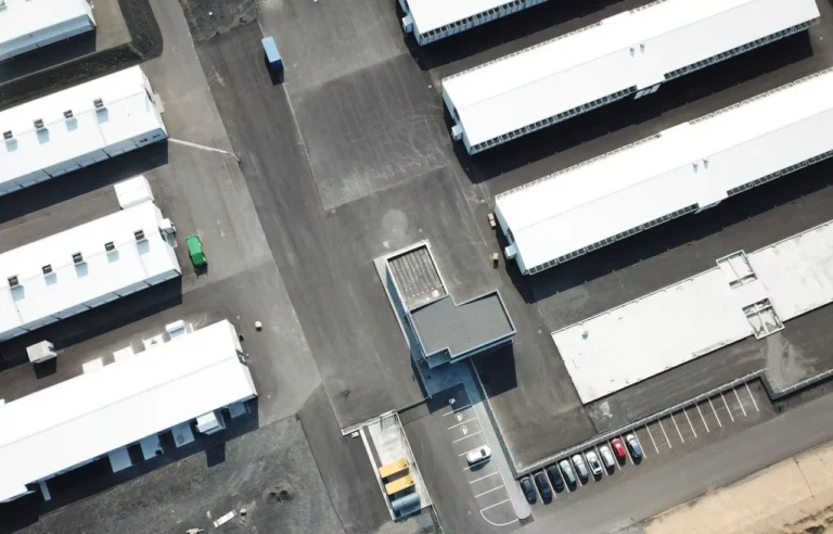 Aerial view of a parking area nestled beside a data center, with several buildings, parked cars, and a few visible trucks.