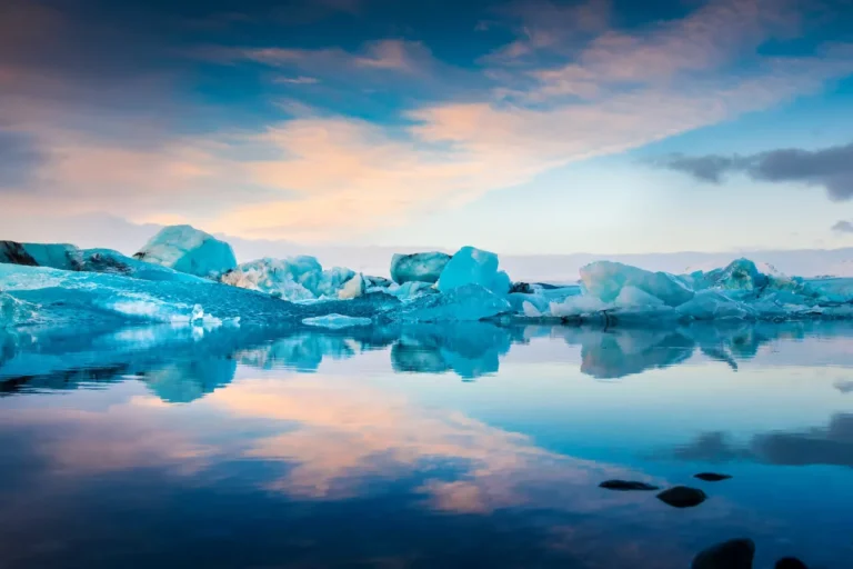 Icebergs float on a calm, reflective body of water under a cloudy sky with hints of pink and blue, resembling the serenity of a data center in perfect harmony.