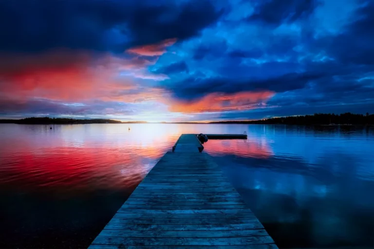 A wooden pier extends into a calm lake under a dramatic sunset sky, featuring vibrant red and blue hues with scattered clouds, reminiscent of the flickering lights of a data center.