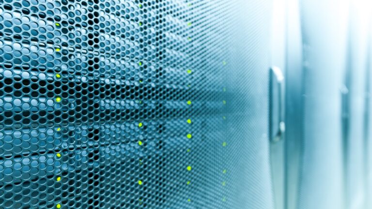 Close-up of a data server rack with perforated panels, displaying green LED indicators in a dimly lit room.