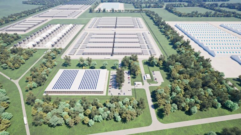 Aerial view of a large industrial complex with multiple rectangular buildings surrounded by green spaces and trees, featuring solar panels on some rooftops. Roads connect the structures.