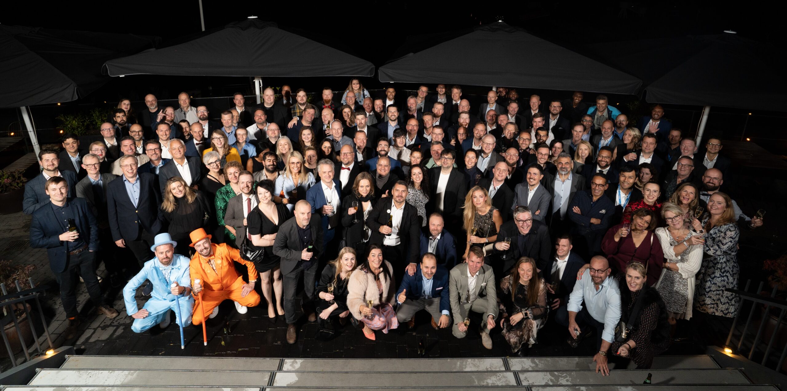Large group of people posing together outdoors at night, dressed in formal attire.