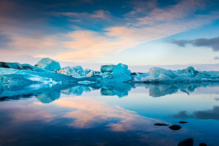 Icebergs floating on calm water under a colorful sunset sky.