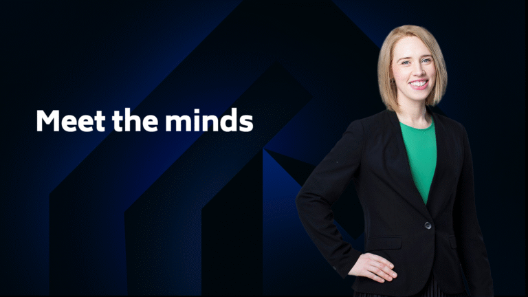 A woman in a black blazer and green top stands smiling next to the text "Meet the minds" on a dark blue geometric background.