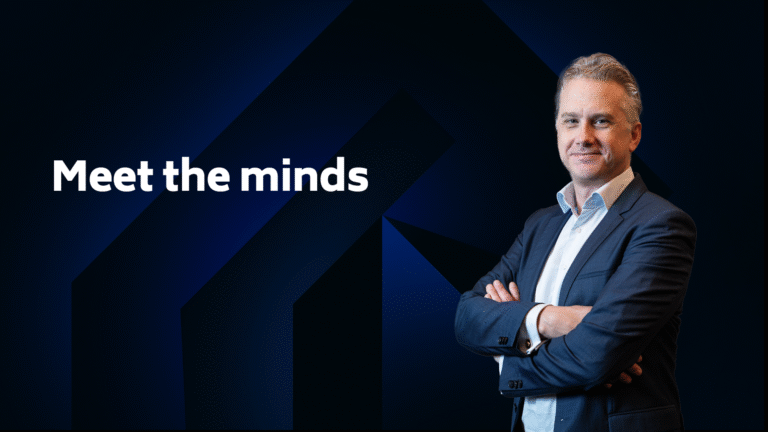 A man in a suit stands with arms crossed next to the text "Meet the minds" on a dark geometric background.
