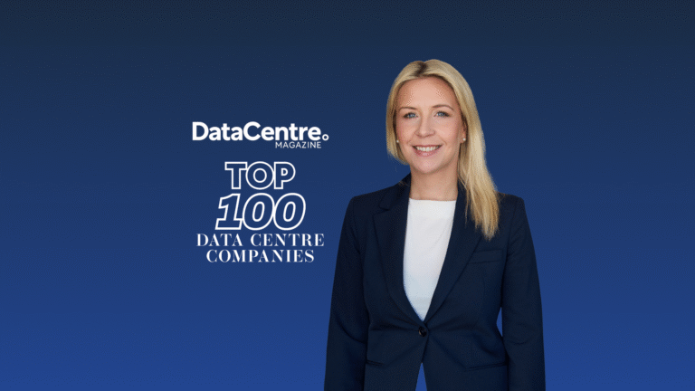 A woman in a navy suit stands in front of a blue background with the text “DataCentre Magazine Top 100 Data Centre Companies.”.