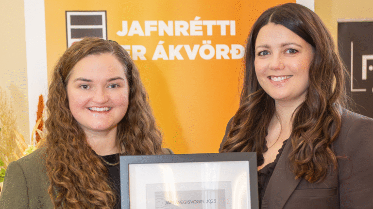Two women stand together, smiling, with one holding a framed certificate. A sign in the background reads "Jafnrétti er ákvörðun.