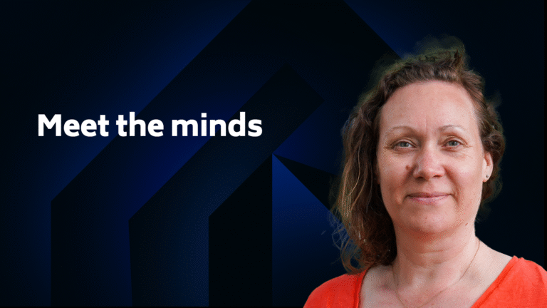 A woman with wavy hair and a coral top stands in front of a dark blue geometric background with the text "Meet the minds.