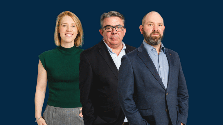 Three people in business attire stand side by side against a solid dark blue background, facing the camera with neutral expressions, embodying leadership and growth in a professional setting.