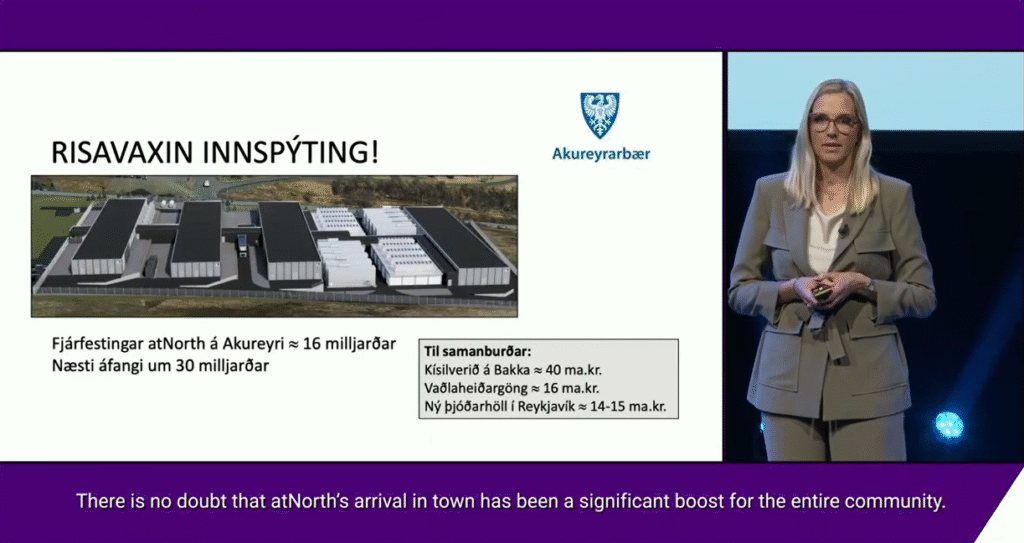 A woman in a suit presents a slide showing an aerial view of a data center project with Icelandic text, charts, and the Akureyri town logo.