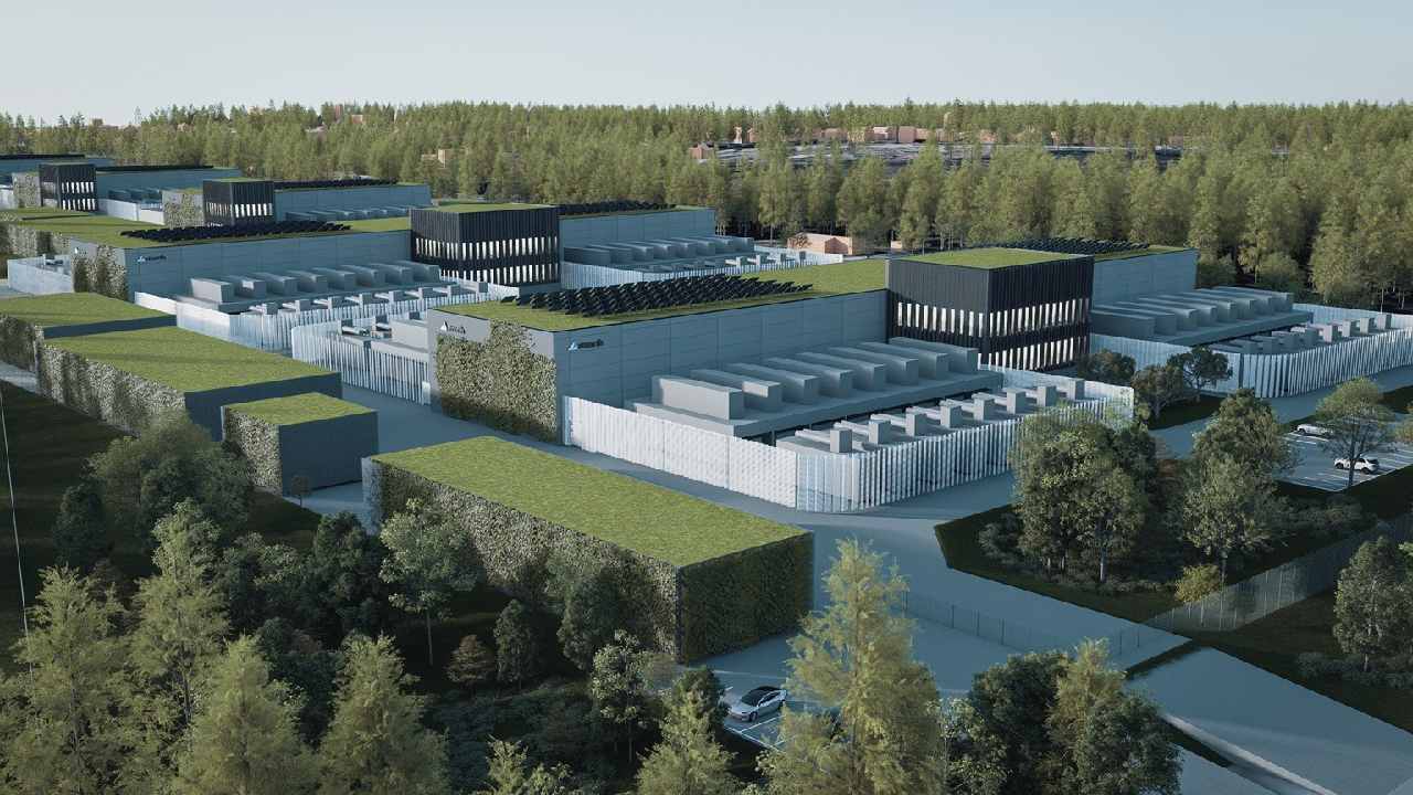Aerial view of a modern data center facility surrounded by trees, featuring multiple rectangular buildings with green rooftops and solar panels.