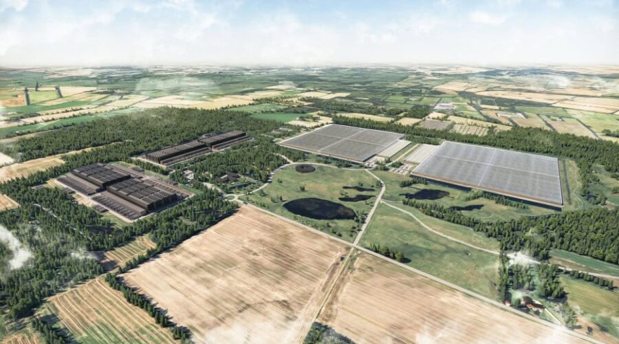 Aerial view of a large industrial complex with several rectangular buildings and surrounding farmland, fields, and patches of forest.