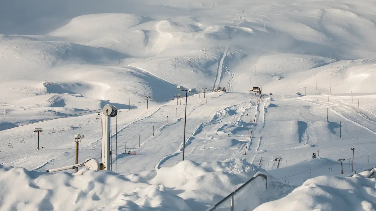 A snow-covered ski resort with multiple ski lifts and tracks set among rolling, white hills under a cloudy sky.