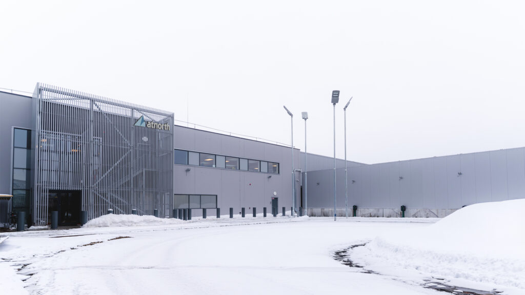 A modern industrial building with large windows and a sign reading "abroth," surrounded by snow on the ground and a cloudy sky overhead.