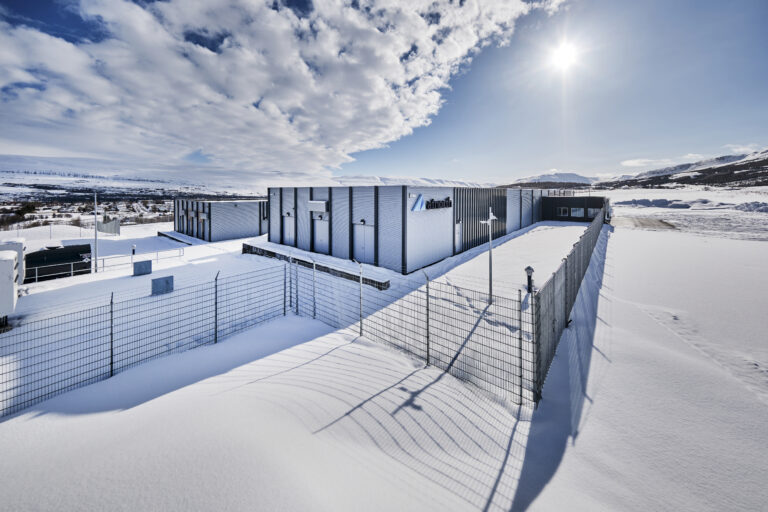 A modern industrial facility, surrounded by snow and a chain-link fence under a bright, partly cloudy sky, exemplifies the next generation of AI-ready data centers.