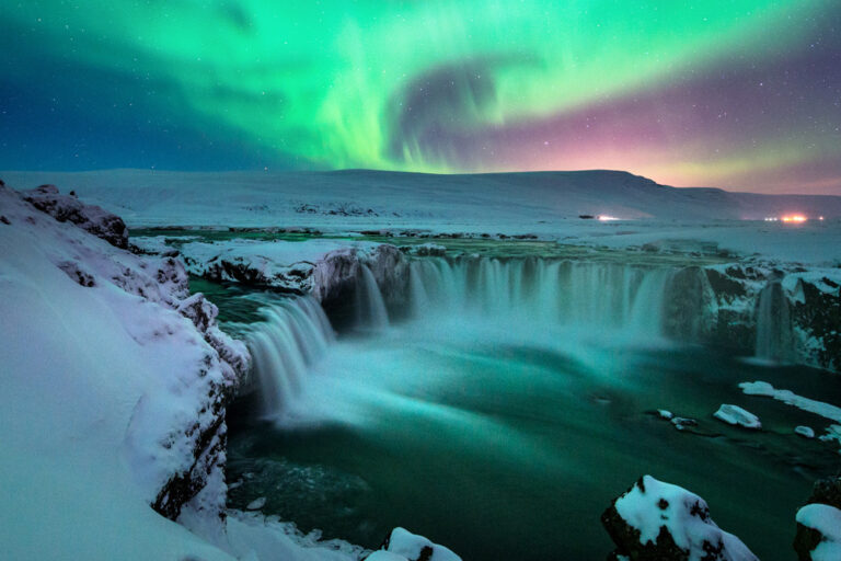 Snow-covered waterfall with green aurora borealis lighting up the night sky, set against a mountainous landscape reminiscent of cutting-edge AI-ready data centers nestled in remote, pristine locations.