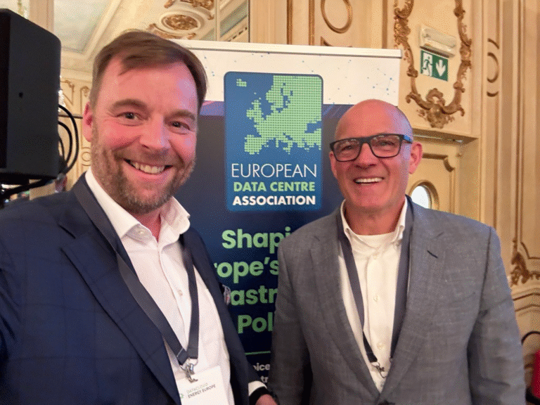 Two men in business attire stand smiling in front of a European Data Centre Association banner at an indoor event.