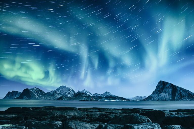 Green aurora borealis lights swirl across a starry night sky above snow-covered mountains and rocky shoreline, echoing the clean energy goals of decarbonizing AI data centers for a brighter, sustainable future.