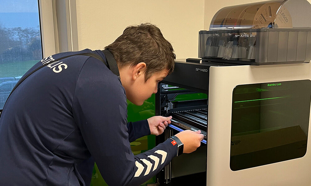 A person loads or adjusts material inside an open 3D printer in a well-lit indoor space.