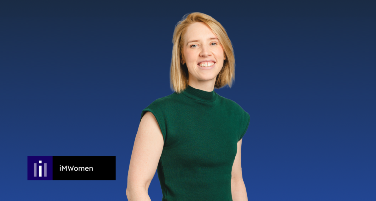 A person with short blonde hair wearing a green sleeveless top stands against a blue background. The iMWomen logo appears in the lower left corner.