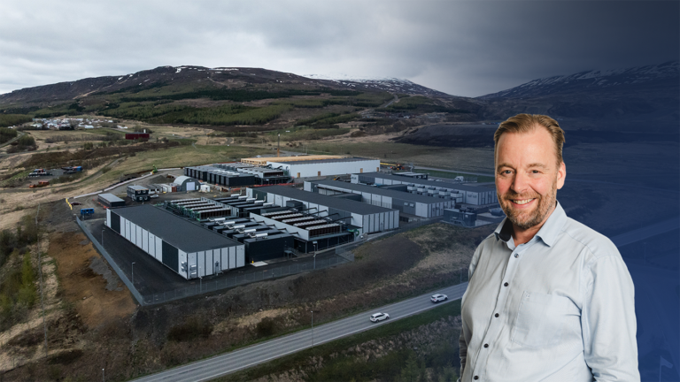 A smiling man in a light blue button-down shirt superimposed over an aerial view of an AI-ready data center near mountains.