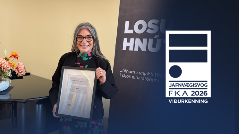 A woman smiling and holding a framed Jafnvægisvog 2026 award certificate next to a branded display stand.